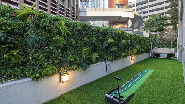 Een moderne stadstuin met een groen gazon, een jeu de boules set en een weelderige verticale geveltuin.