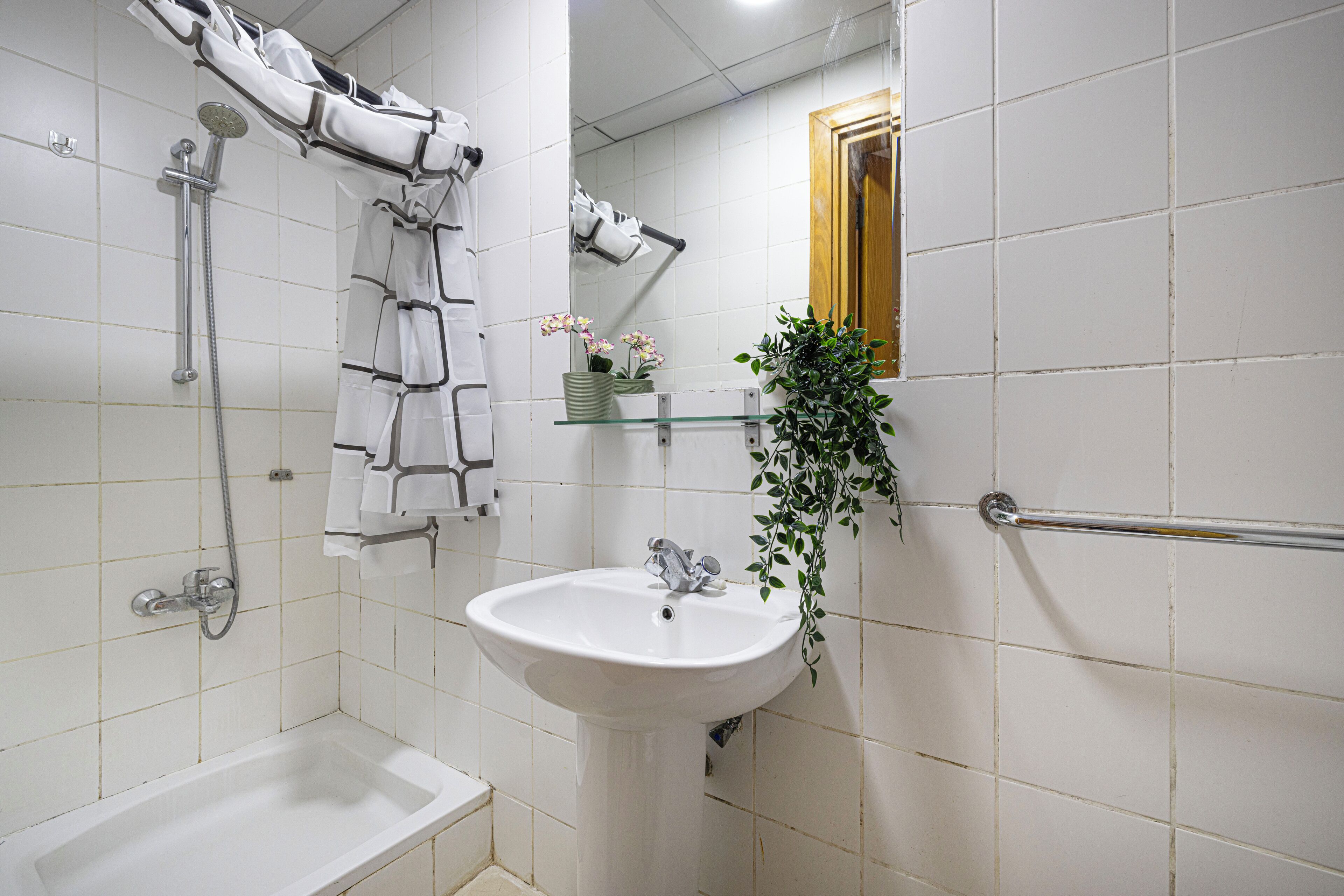 Ein Badezimmer mit einem weißen Waschbecken, einer Dusche und einer Badewanne. Es gibt einen Handtuchhalter, einen Spiegel und eine Topfpflanze.