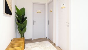 Een gang met witte deuren, een houten bankje en een grote groene plant.