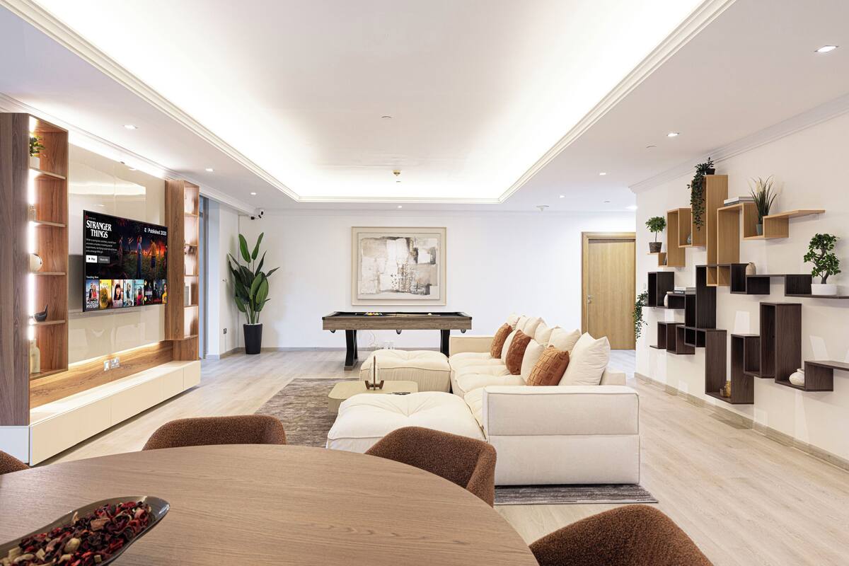 Een moderne woonkamer met een bank, salontafel en een pooltafel. Links een televisie en rechts een boekenkast.