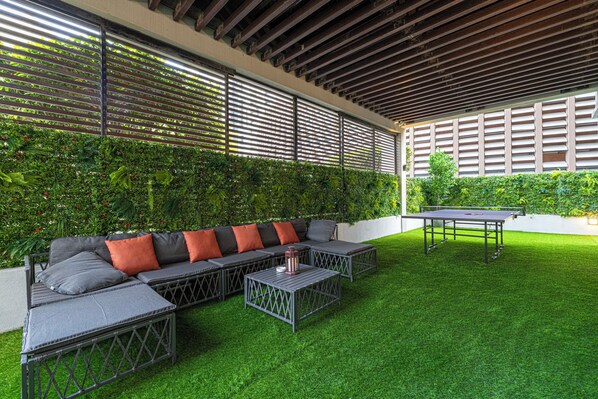 A covered outdoor seating area with a sectional sofa, a coffee table, and a ping pong table.