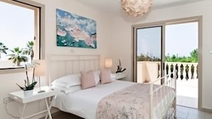 Une chambre à coucher avec un lit, des tables de chevet, une fenêtre et un balcon offrant une vue.