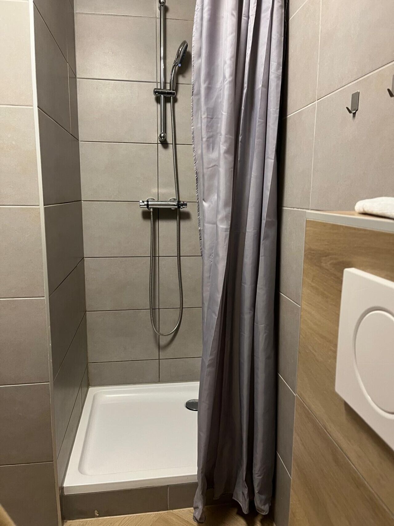 Ein Duschbereich mit einer weißen Badewanne, einem grauen Duschkopf und einem grauen Duschvorhang.