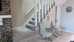A living room with a staircase, a brick wall, a glass table, and a chair. - Rusty Turtle Beach House (Myrtle Beach)