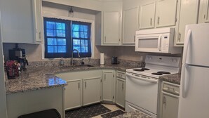 A kitchen with white cabinets, a microwave, a stove, and a sink. - Rusty Turtle Beach House (Myrtle Beach)