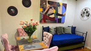 Et værelse med en seng, et bord med stole, en blomstervase og et billede på væggen.