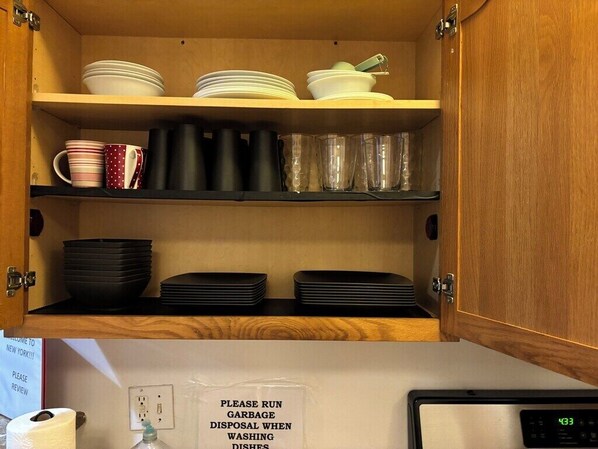 A kitchen with wooden cabinets, shelves with dishes, and a sign instructing to run garbage disposal when washing dishes.