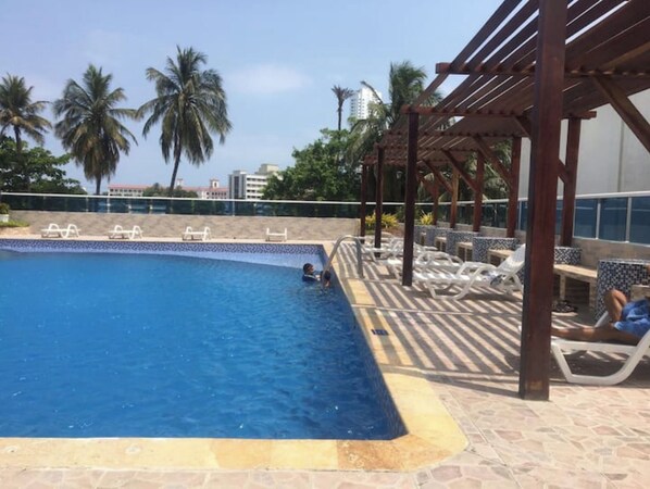 Relax by the pool surrounded by palm trees and a shaded seating area.