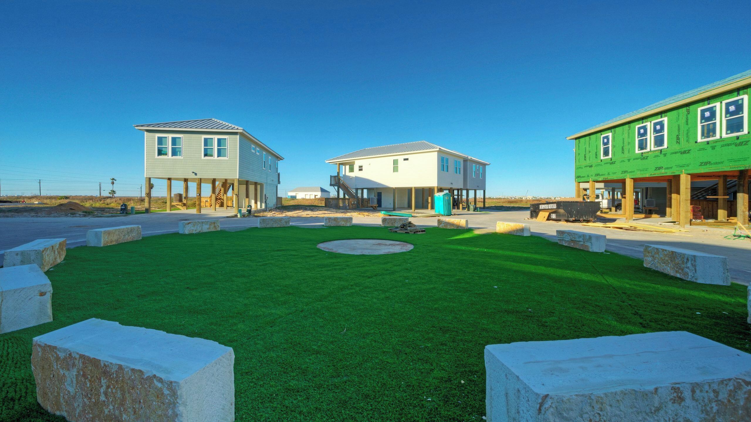 A residential area with three houses, a grassy lawn, and a clear sky.