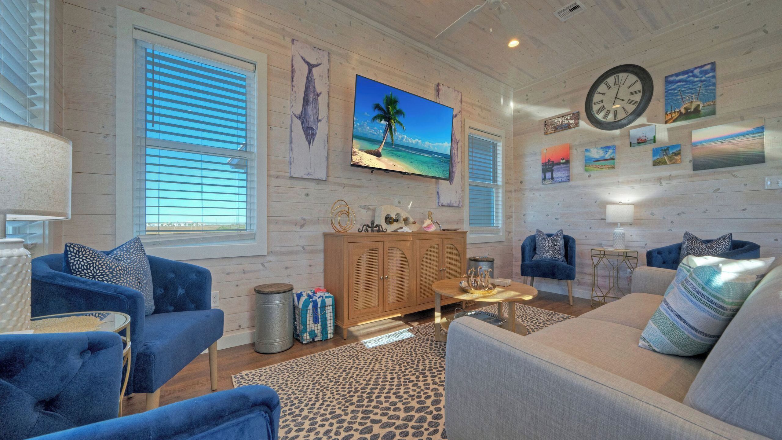 A living room with a wooden wall, a large clock, and a beach-themed painting.
