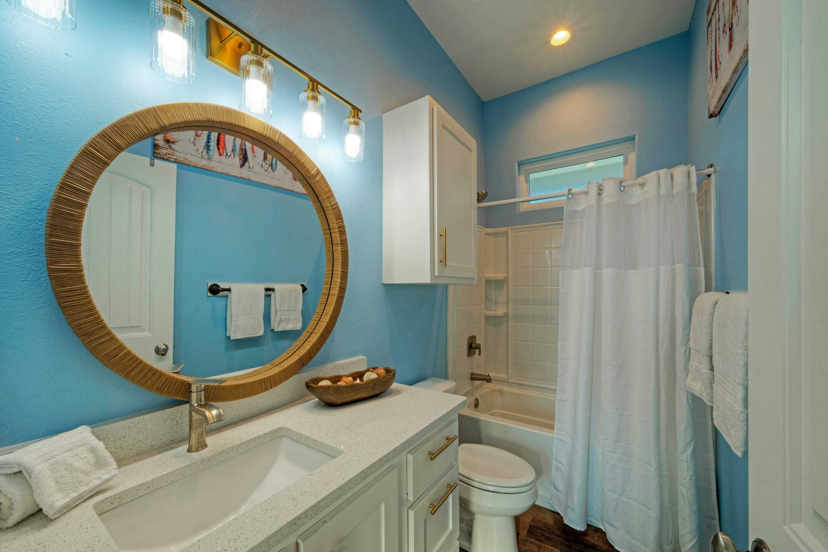 A bathroom with a blue wall, a white sink, a large mirror, and a bathtub.