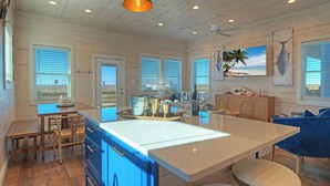 A spacious kitchen with a large island, wooden cabinetry, and a view of the beach through the windows.
