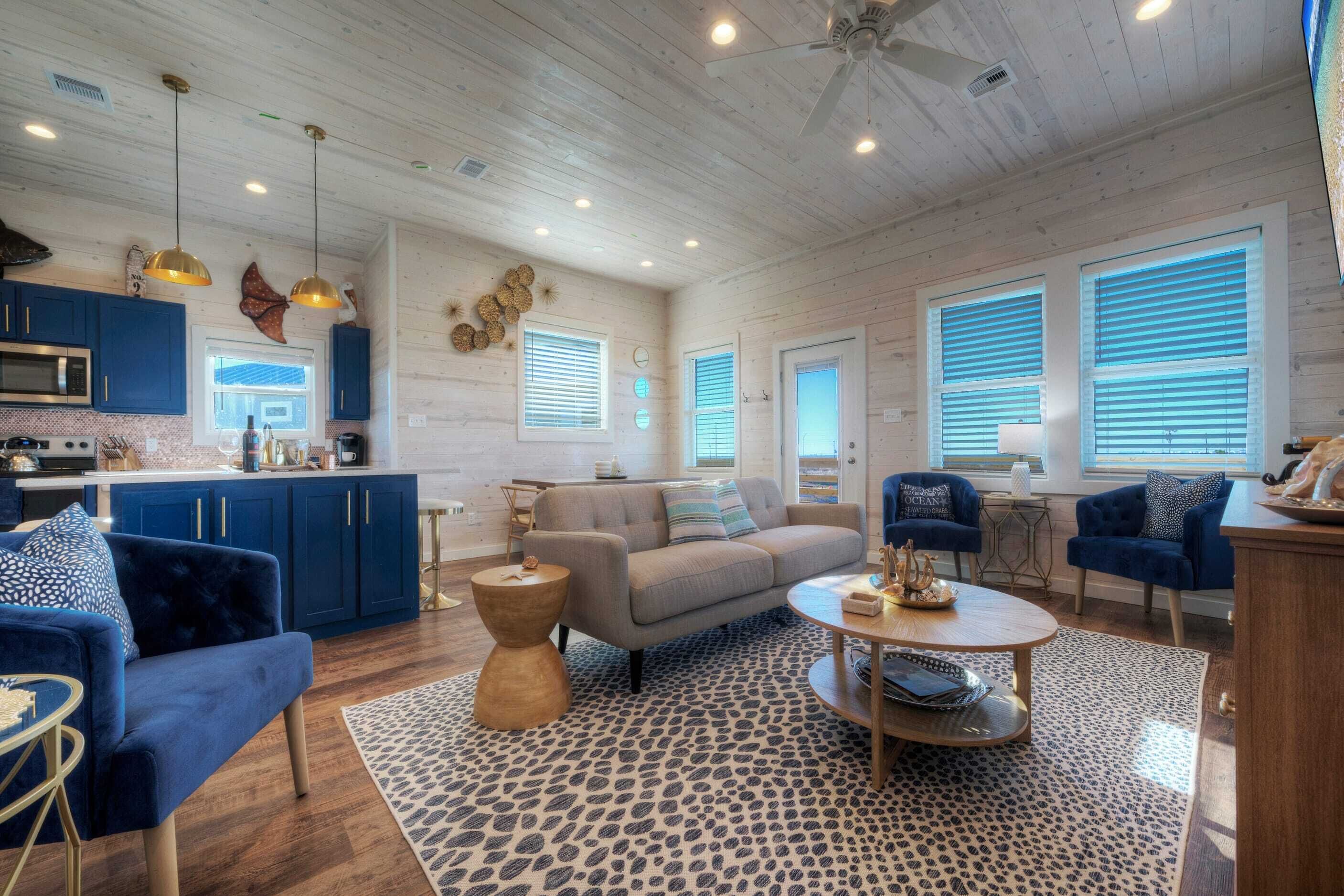 A spacious living area with a sofa, two armchairs, a coffee table, and a kitchen area with blue cabinets and a microwave.