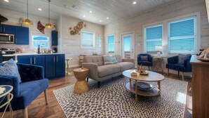 A spacious living area with a sofa, two armchairs, a coffee table, and a kitchen area with blue cabinets and a microwave.