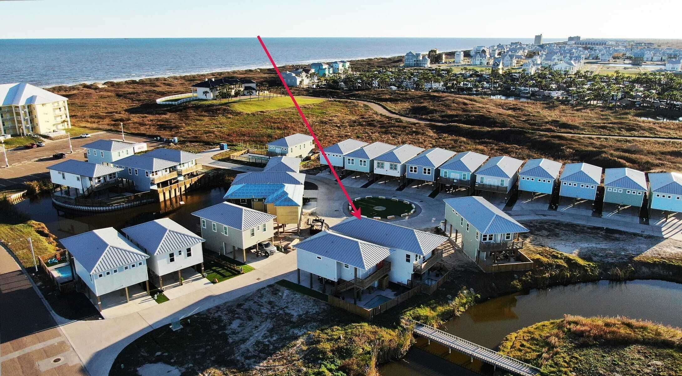 Un complejo turístico en la costa con varias edificaciones tipo cabaña, una piscina central y vistas al océano.