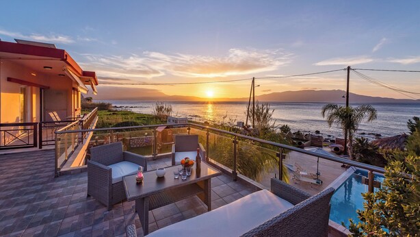 A balcony with wicker furniture, a pool, and a view of the ocean at sunset.