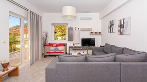 A modern living room with a grey sofa, a television, and a dining area with a red and white table.