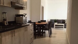 A modern kitchen with wooden cabinets, a dining area with a table and chairs, and a living room with a sofa and coffee table.