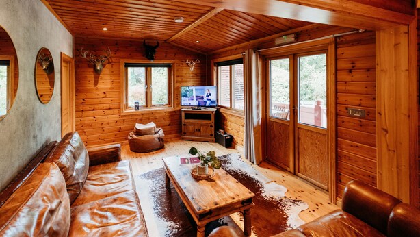 Ein Holzblockhaus-Interieur mit Ledersofa, Holztisch und Fernseher.