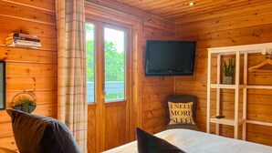 Um quarto de cabana de madeira aconchegante, com uma cama, uma televisão na parede e uma janela com cortinas.