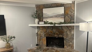 A stone fireplace with a mantel shelf, a flat-screen TV mounted on the wall, and a lamp on a side table. - Masters 2026 Rental! 3 Bed 2 Bath! (Martinez)