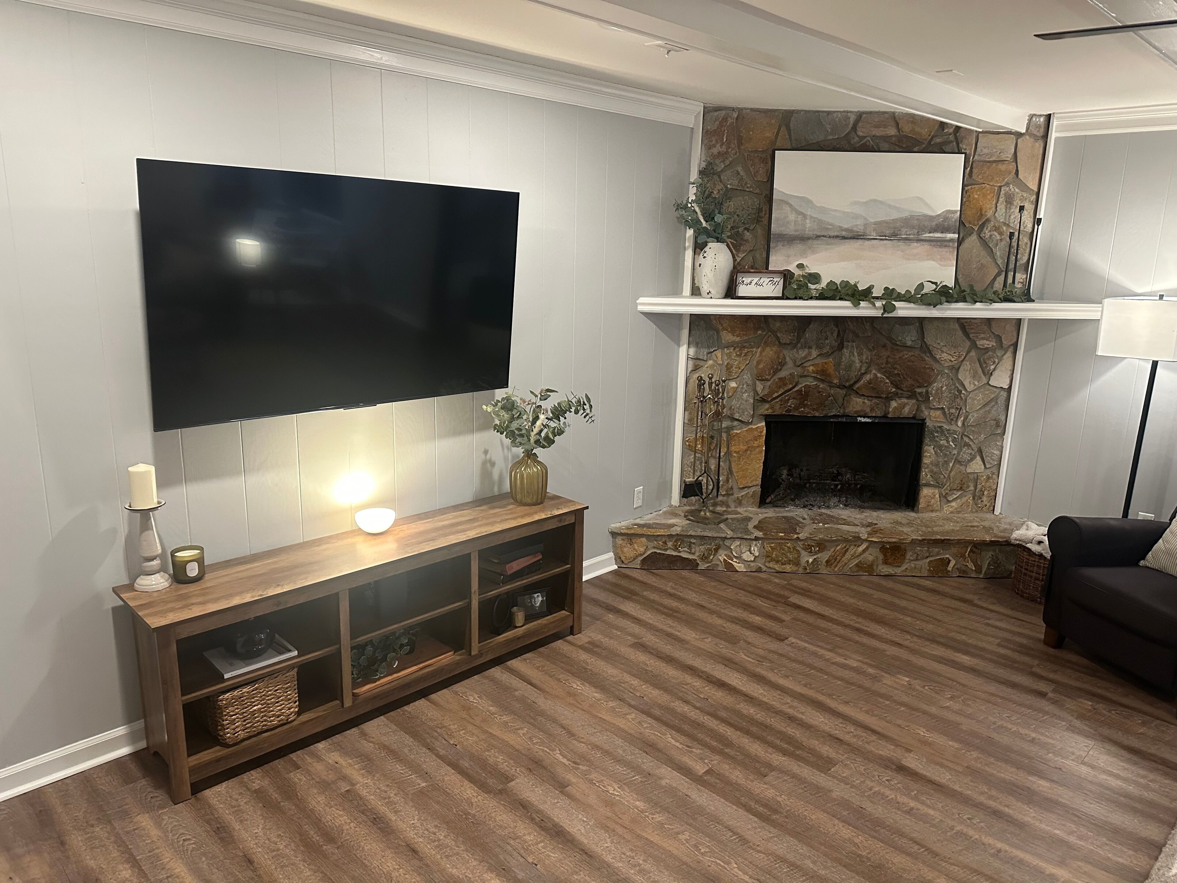 Ein Wohnzimmer mit flachbildfernseher an der Wand, einem Kamin aus Stein mit Kaminfeuerholzablage und einer Holzunterhaltungsecke.