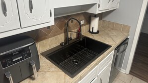 A kitchen with white cabinets, a black sink, a dishwashing machine, and a paper towel holder. - Masters 2026 Rental! 3 Bed 2 Bath! (Martinez)