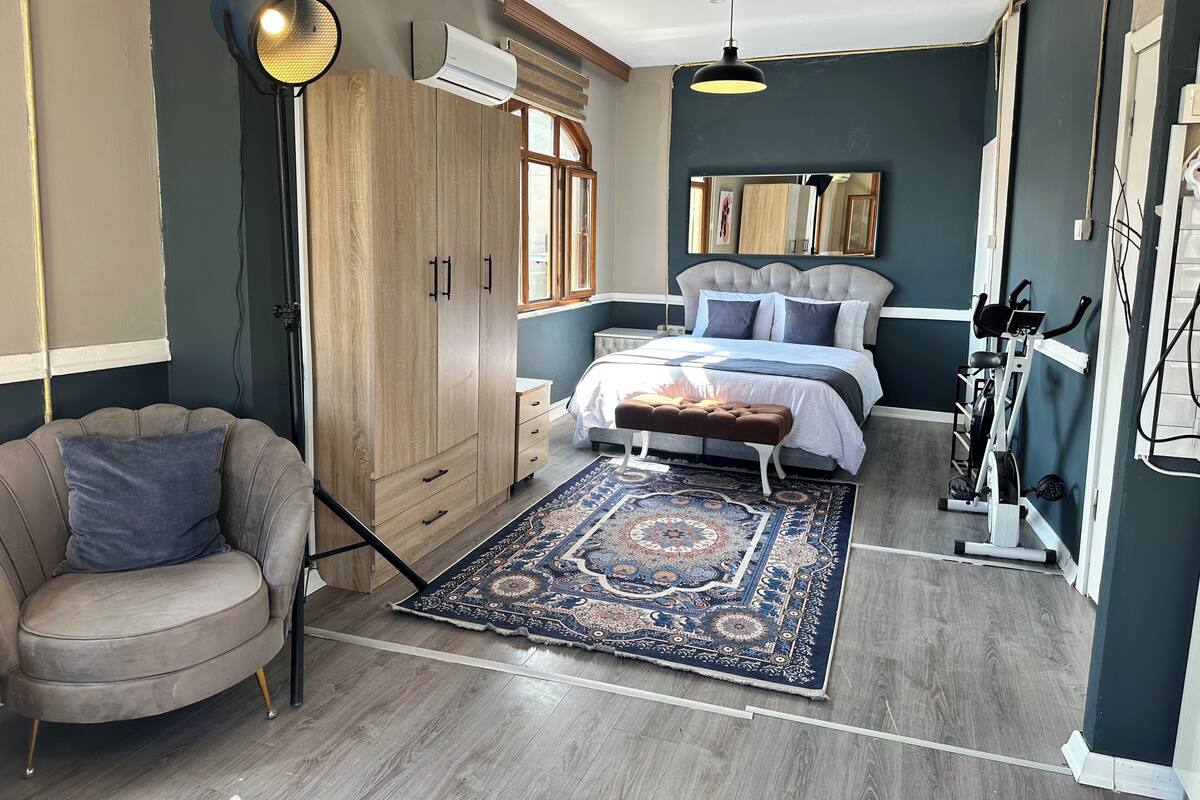 Ein Schlafzimmer mit einem Bett, einer Kommode, einem Kleiderschrank, einer Stehlampe und einem Heimtrainer.