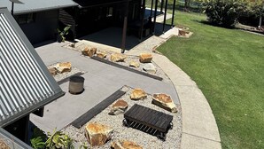 A covered outdoor seating area with a grill, surrounded by a landscaped garden with rocks and a lawn. - Unique rural cabin, 5 minutes from beach (Valla)