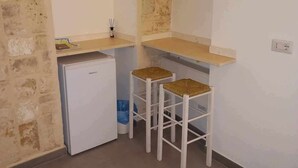 Une cuisine de taille réduite, équipée d’un réfrigérateur, de deux tabourets et d’un petit plan de travail.