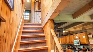Un escalier en bois mène à une cuisine dotée de meubles de rangement en bois et d’un îlot central.