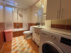 Une salle de bain équipée d’une douche, de toilettes, d’un lavabo et d’un lave-linge.