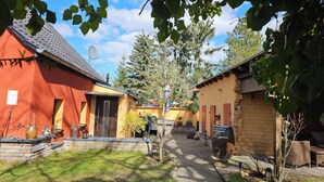 A courtyard with a stone pathway, a small tree, and a rustic building with a tiled roof. - Kleine Perle am Schwielowsee (Schwielowsee)