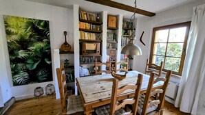 A dining area with a wooden table and chairs, surrounded by bookshelves filled with books and decorative items. - Kleine Perle am Schwielowsee (Schwielowsee)