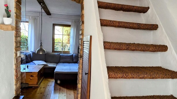A staircase with wooden steps and a brick archway leading to a living area with a sofa and a window. - Kleine Perle am Schwielowsee (Schwielowsee)