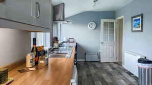 A modern kitchen with a wooden countertop, stainless steel appliances, a clock, and a door leading to another room. - Six the Square - UK48869 (Belford)