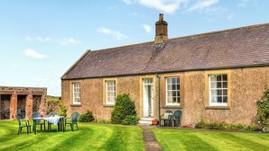 A brick house with a well-maintained lawn, a dining area with chairs and a table, and a chimney. - Six the Square - UK48869 (Belford)