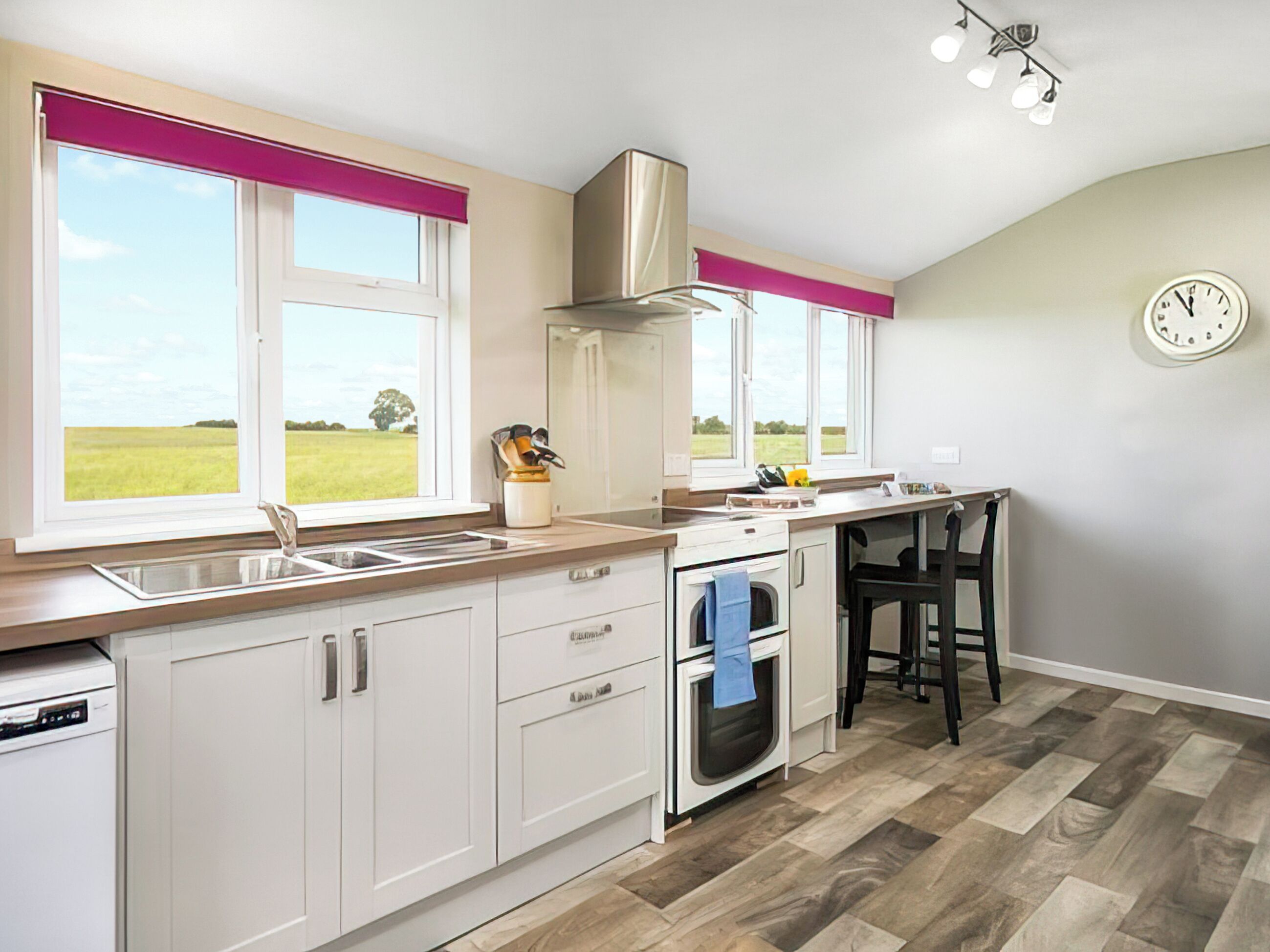 A modern kitchen with white cabinets, a built-in oven, a gas stove, and a window with a view of a green field.
