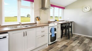 A modern kitchen with white cabinets, a built-in oven, a gas stove, and a window with a view of a green field. - Six the Square - UK48869 (Belford)
