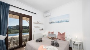 Ein Schlafzimmer mit Bett, Meerblick, einem Gemälde und einem Fenster mit Vorhängen.