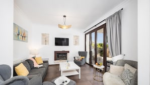 Ein modernes Wohnzimmer mit grauen Sofas, einem weißen Couchtisch, einem Kamin, einem Fernseher und einer großen Glasschiebetür zum Außenbereich.