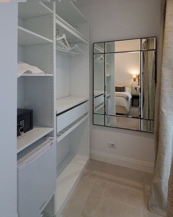 A walk-in closet with open shelving, a mirror, and a bed in the adjacent room.