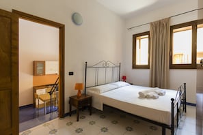Ein Schlafzimmer mit einem Bett, einem Nachttisch, einer Lampe, einem Sessel, einem Schreibtisch, einem Spiegel und einem Fenster mit Vorhängen.