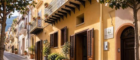 Une rue bordée d’immeubles jaunes, de volets en bois et de balcons ornés de plantes en pot.