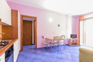 Eine kleine Küche mit Herd, Spüle und Schränken, ein Essbereich mit Tisch und Stühlen sowie ein Fernseher auf einem Schrank.