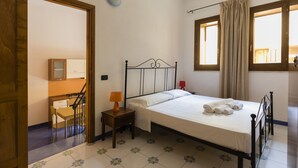 Une chambre à coucher comprenant un lit, une table de chevet, une lampe, une chaise, un bureau, un miroir et une fenêtre avec des rideaux.
