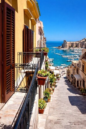 Una calle estrecha con balcones, plantas en macetas y vistas al mar y barcos.