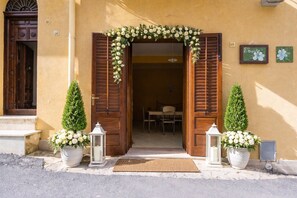 A building entrance with a wooden door, a doormat, and two potted plants.