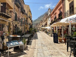 A narrow street with outdoor seating, shops, and a mountain backdrop.