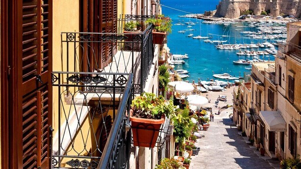 A narrow street with balconies, potted plants, and a view of the sea and boats. - Visitsicilia Le Magnolie 4 (Castellammare del Golfo)